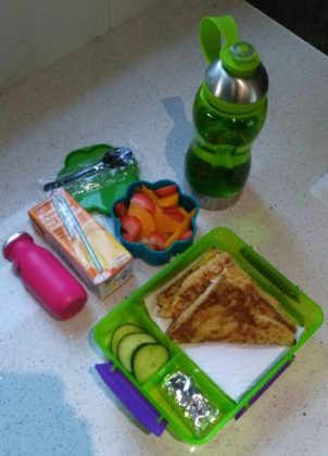 Savoury egg bread, cucumber slices, cereal bar, fruit salad, jelly , juice, drinking yoghurt and water bottle